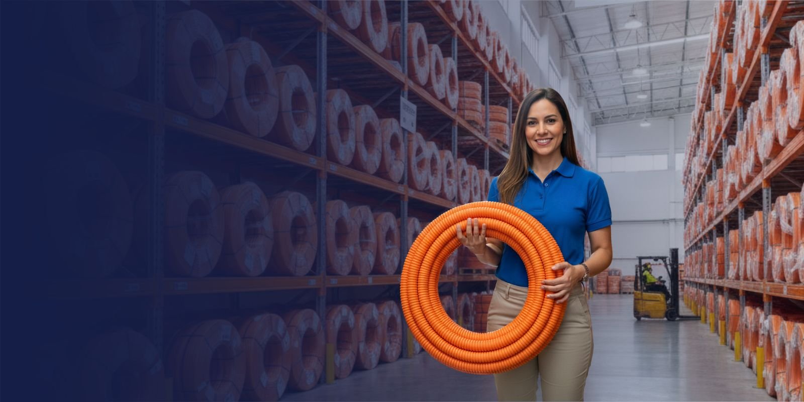 Mujer sonriente de Karrasa con camisa azul, sosteniendo un rollo de poliducto naranja en un almacén de materiales eléctricos.